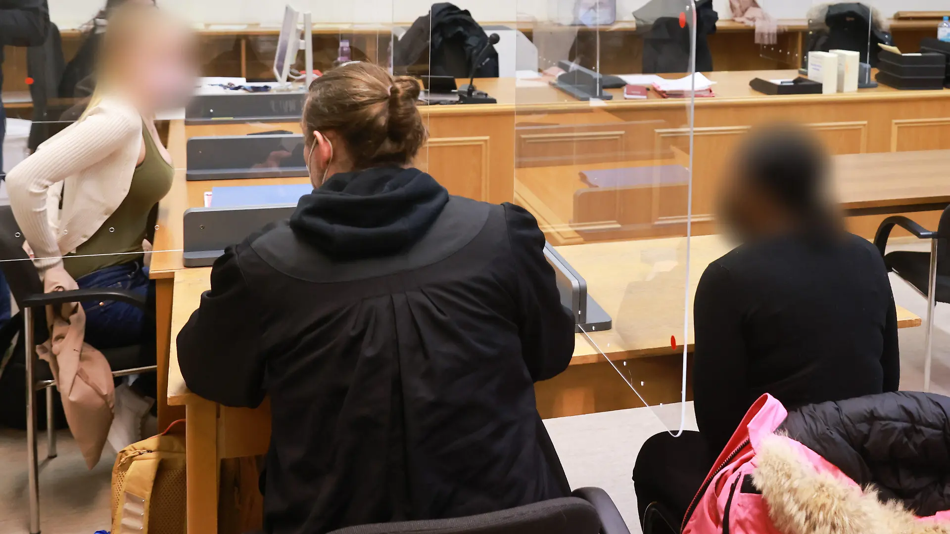 03.02.2022, Hamburg: Zwei angeklagte Frauen warten in einem Gerichtssaal im Strafjustitzgebäude in Hamburg auf den Beginn der Verhandlung. Mittig sitzt ein Anwalt. Die beiden Frauen sollen unter anderem im Juli 2019 einem Kunden Geld, Handy und Bankkarten abgenommen haben. Foto: Ulrich Perrey/dpa - ACHTUNG: Person(en) wurde(n) aus rechtlichen Gründen gepixelt +++ dpa-Bildfunk +++