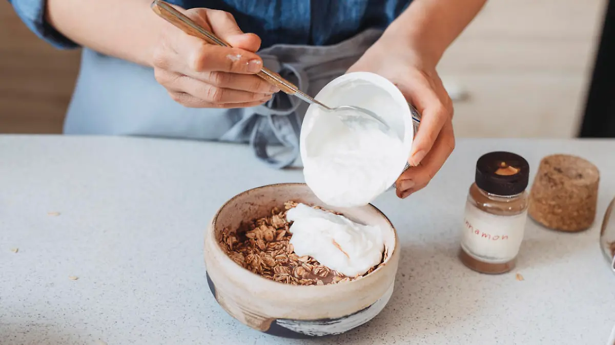 Making breakfast: unrecognizable woman adding yoghurt to oatmeal.