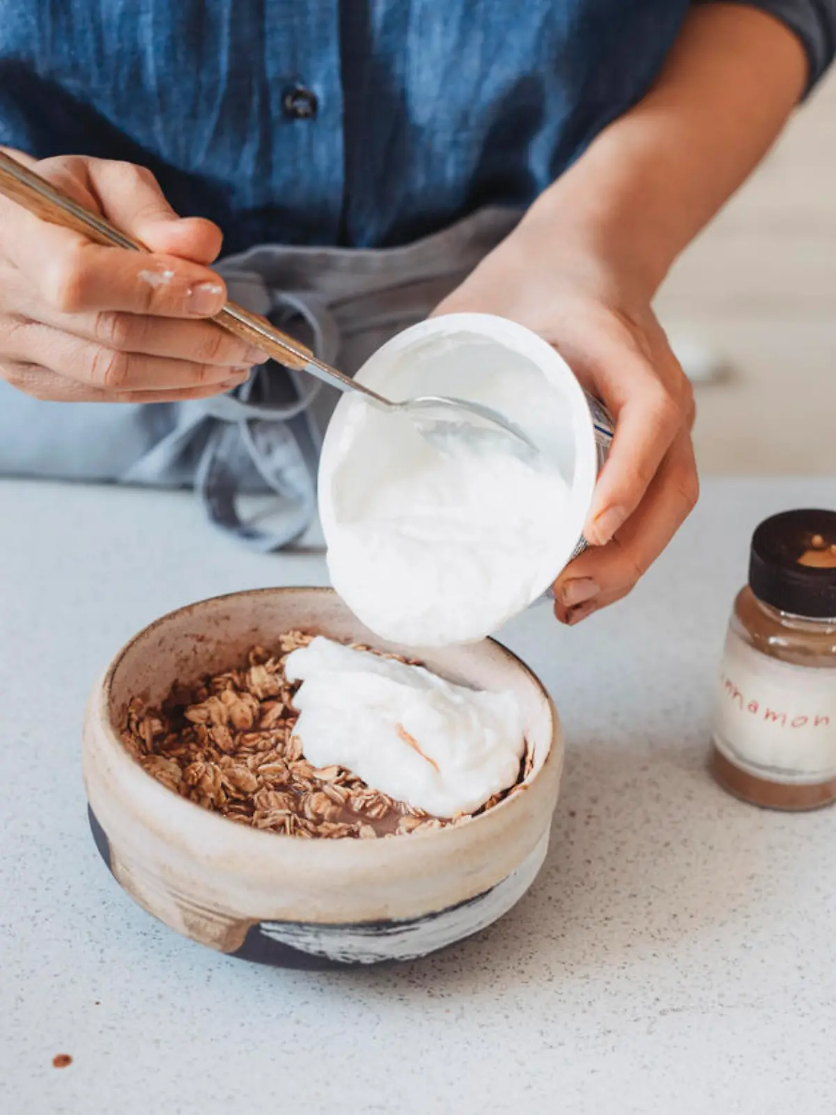 Making breakfast: unrecognizable woman adding yoghurt to oatmeal.
