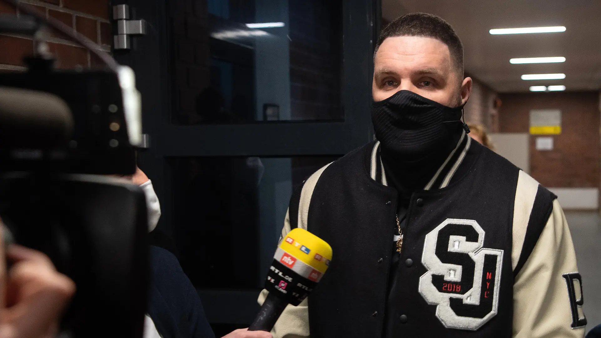 15.01.2021, Berlin: Rapper Fler, bürgerlich Patrick Losensky, gibt auf dem Weg zum Gerichtssaal einem Fernsehsender ein Interview. Dem 38-Jährigen werden Beleidigung, Sachbeschädigung, versuchte Nötigung und Fahren ohne Fahrerlaubnis vorgeworfen. Immer wieder soll der Musiker verschiedene Menschen wüst verunglimpft und beleidigt haben. Das Verfahren hatte bereits im November 2020 begonnen, musste dann aber wegen Erkrankung des Angeklagten ausgesetzt werden. Foto: Paul Zinken/dpa-Zentralbild/dpa +++ dpa-Bildfunk +++