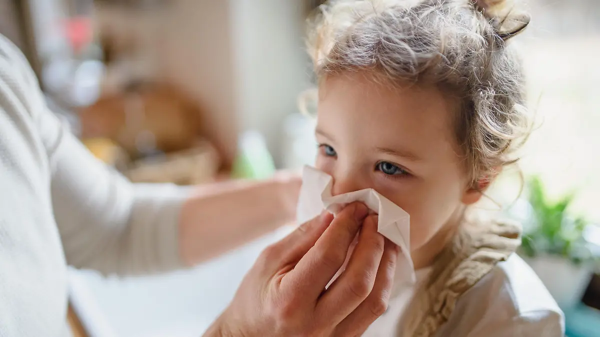 Unrecognizable father with small sick toddler daughter indoors at home, blowing nose.
