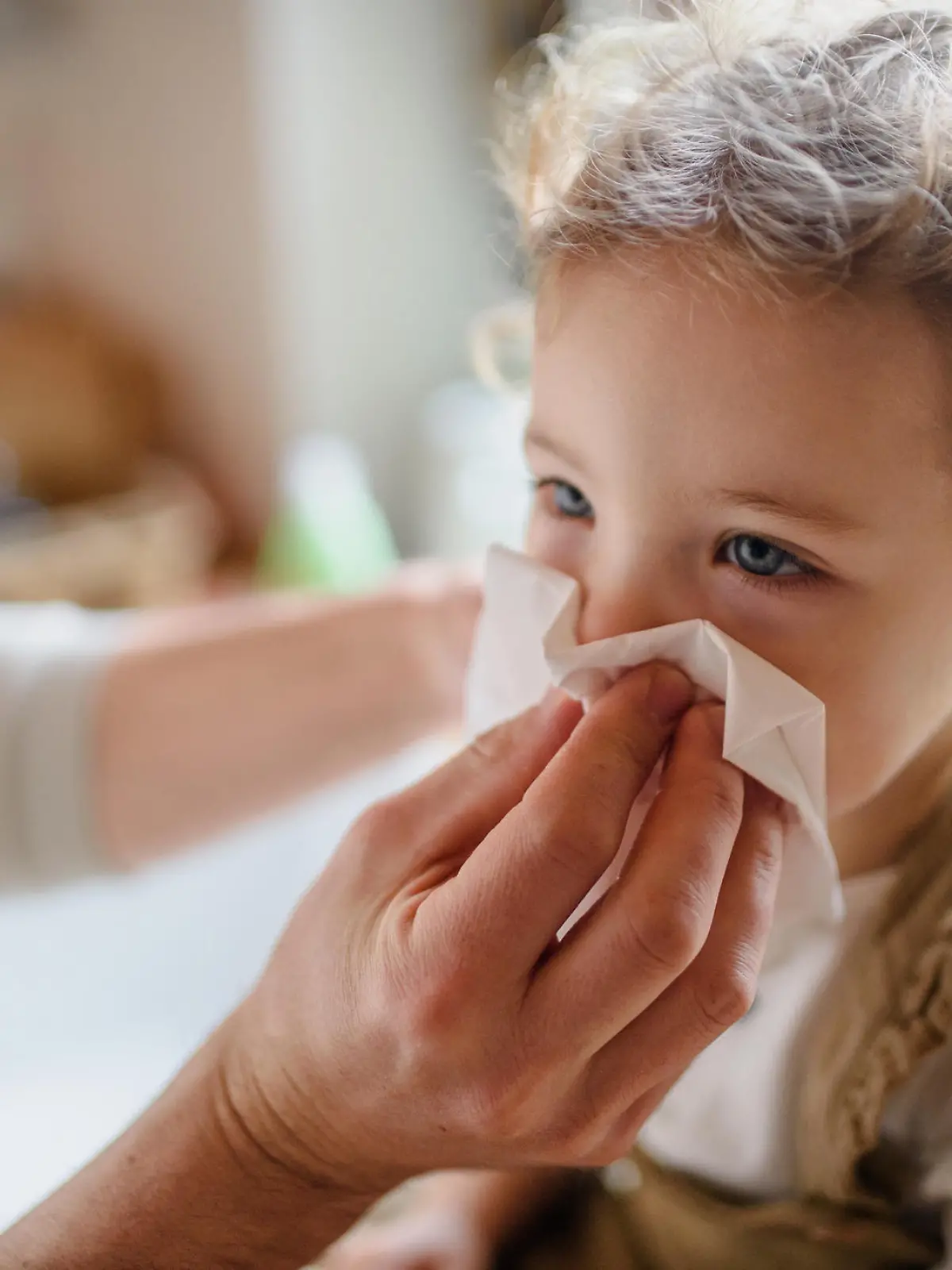 Unrecognizable father with small sick toddler daughter indoors at home, blowing nose.