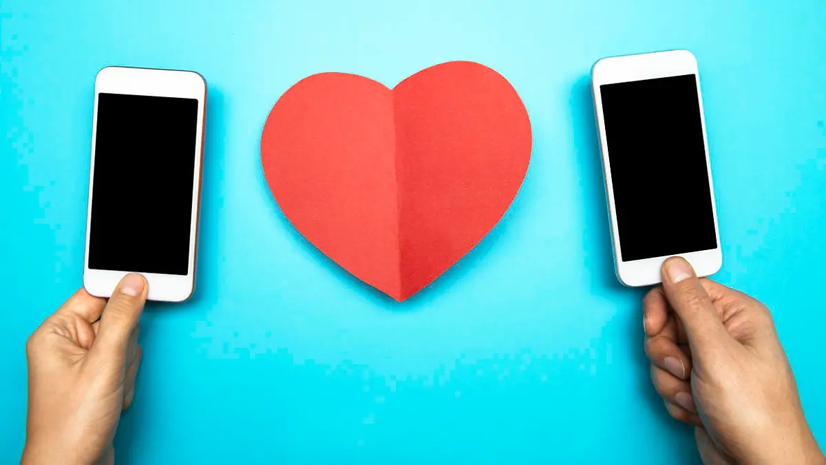 Two hands holding smart phones and a red heart shape on blue background. Representing online dating mobile applications.