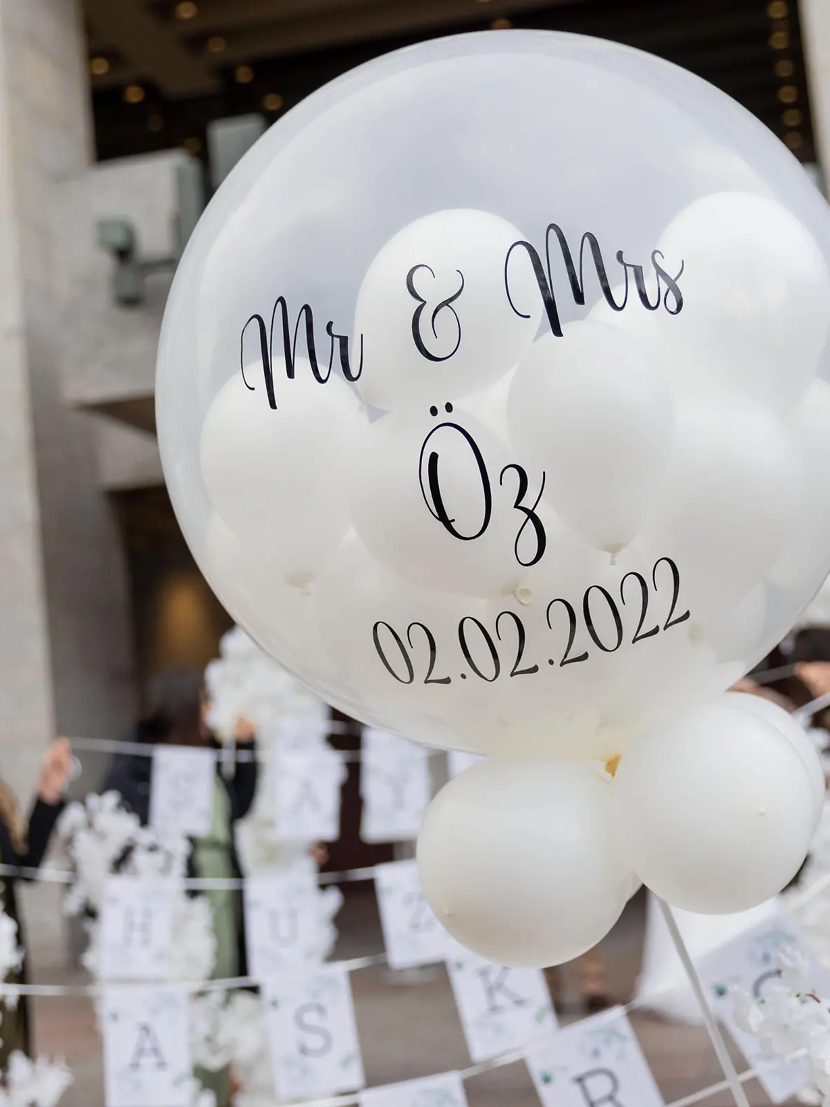 "Mr & MRS Öz und 02.02.2022" steht auf einem Luftballon einer Hochzeitsgesellschaft vor dem Standesamt.