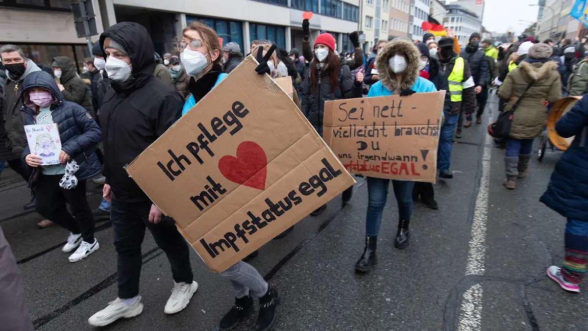 Ein Banner „Ich pflege mit Herz - Impfstatus egal“ wird vom Demonstrant einer Versammlung gehalten. Die Teilnehmer demonstrieren gegen die Corona-Politik.