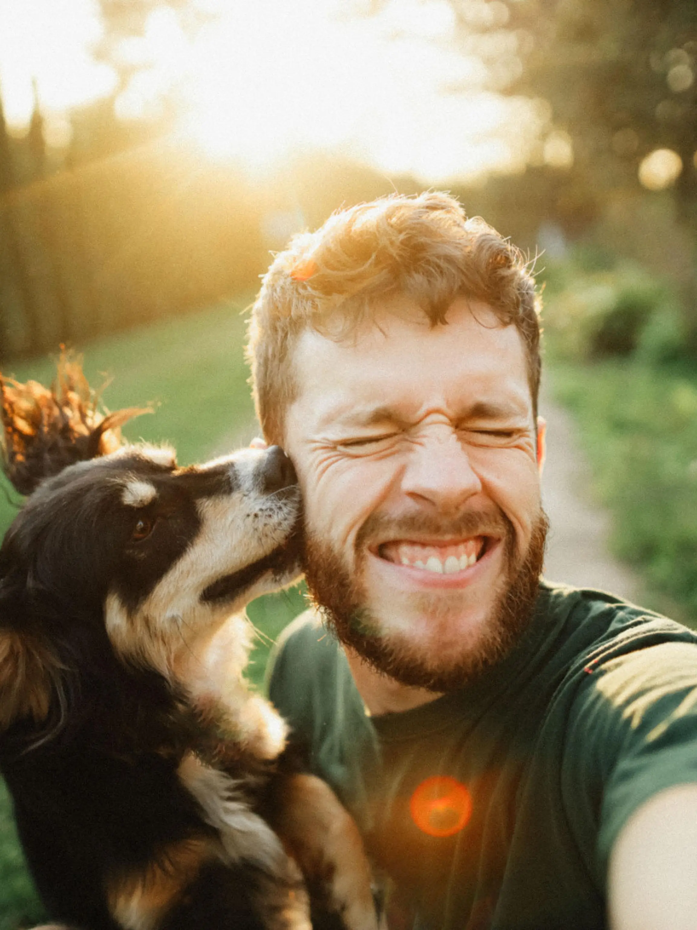 Selfie of a young handsome man with his dog on the green yard in the countryside at the sunset on summer