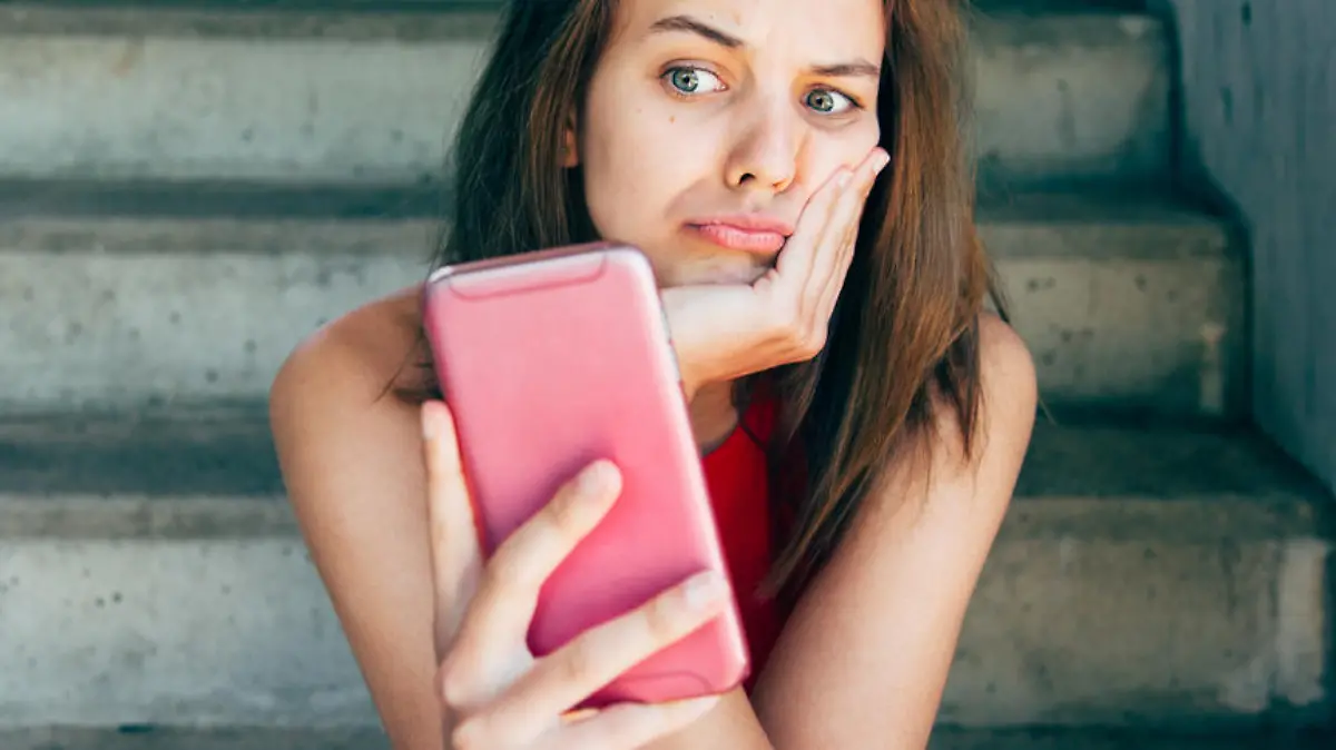Displeased teen girl looking at her smartphone sitting on the stairs outdoors
