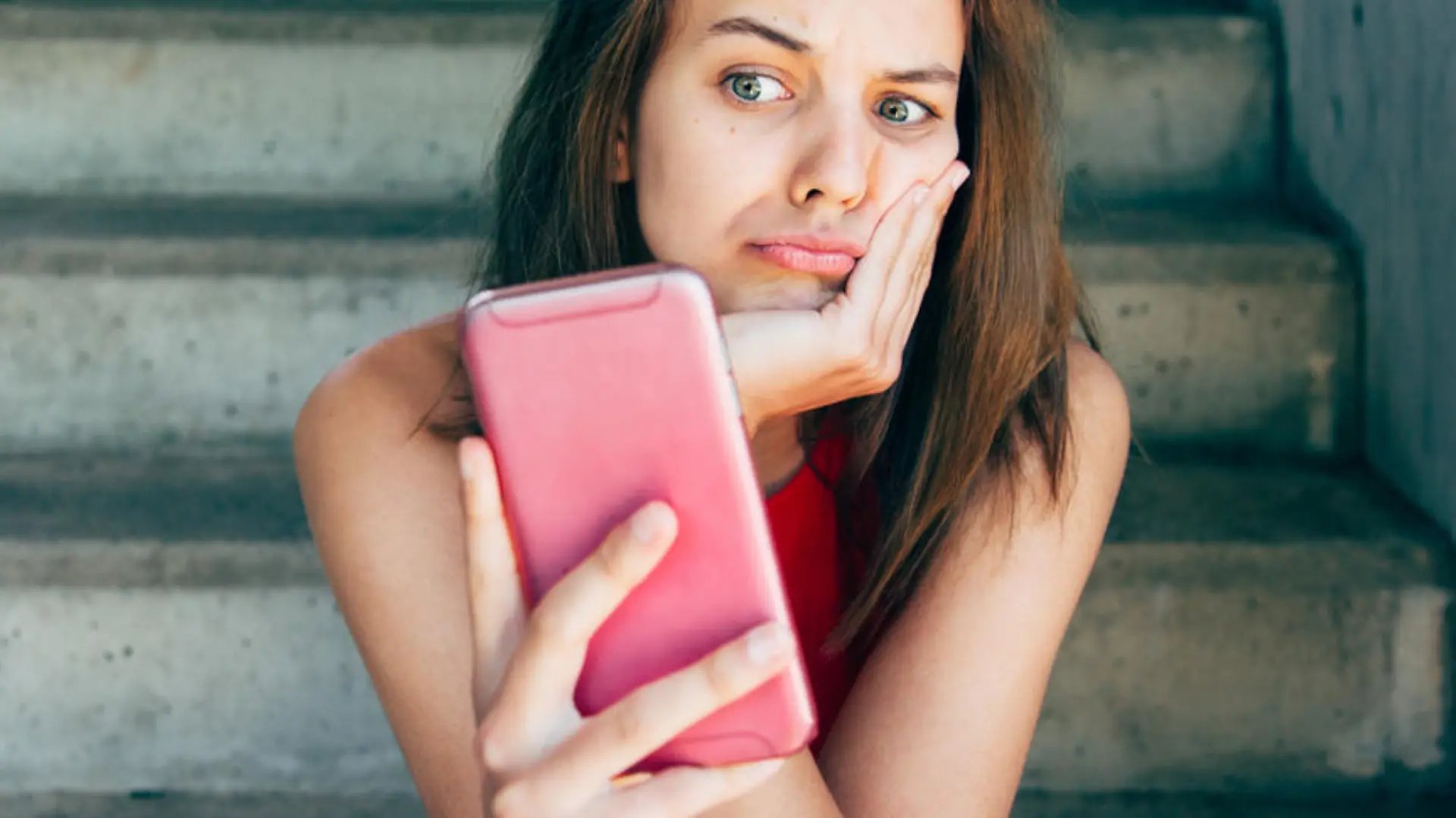 Displeased teen girl looking at her smartphone sitting on the stairs outdoors