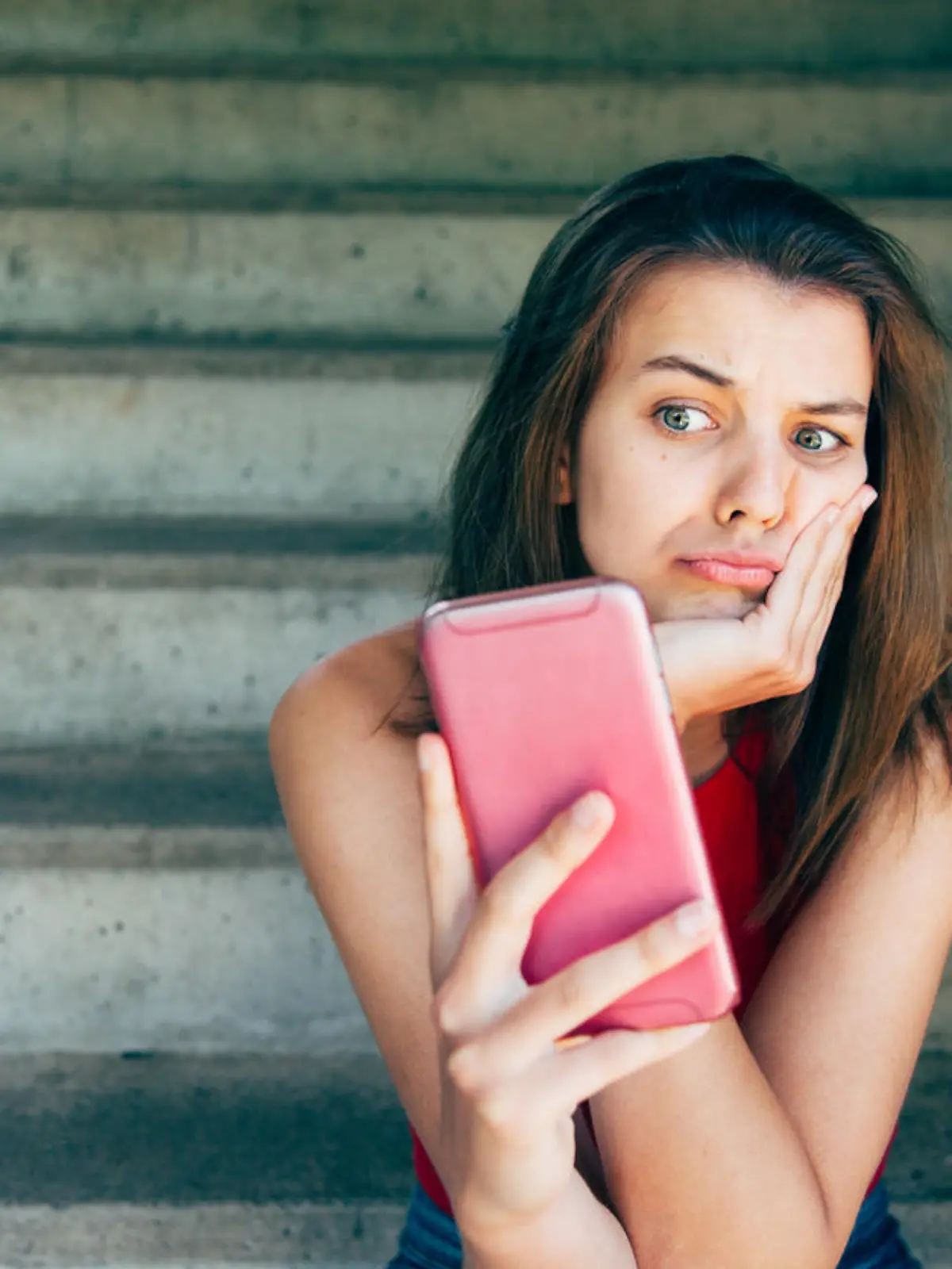 Displeased teen girl looking at her smartphone sitting on the stairs outdoors
