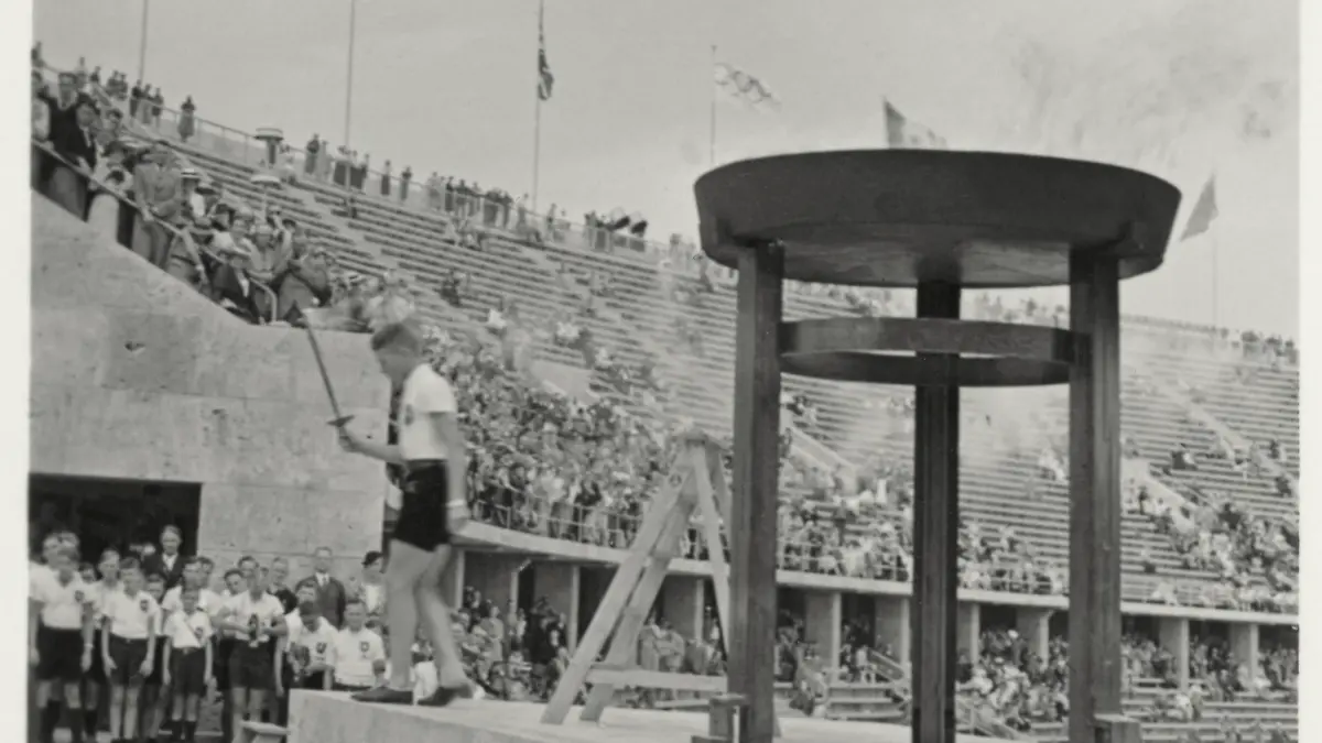 IX. Olympische Spiele / Sommerspiele / Berlin, 1. August bis 16. August 1936 / Staffellauf der Berliner Sportjugend zum Austragungsort der olympischen Ruder- und Kanuten-Wettbewerbe in Grünau, 7. August. - "Berlin: Die Jugend holt das Olympische Feuer zum Staffellauf nach Grünau". - (Entzünden der ersten Fackel an der Olympischen Flamme über dem Marathon-Tor im Berliner Olympiastadion). Foto (Teil einer stereoskopische Aufnahme) von Heinrich Hoffmann (1885-1957). Aus: Die Olympischen Spiele 1936. 100 Raumbild-Aufnahmen von Heinrich Hoffmann. Text von Ludwig Haymann, Diessen am Ammersee (Raumbild-Verlag Otto Schönstein) 1936, Nr. 43. Privatsammlung.