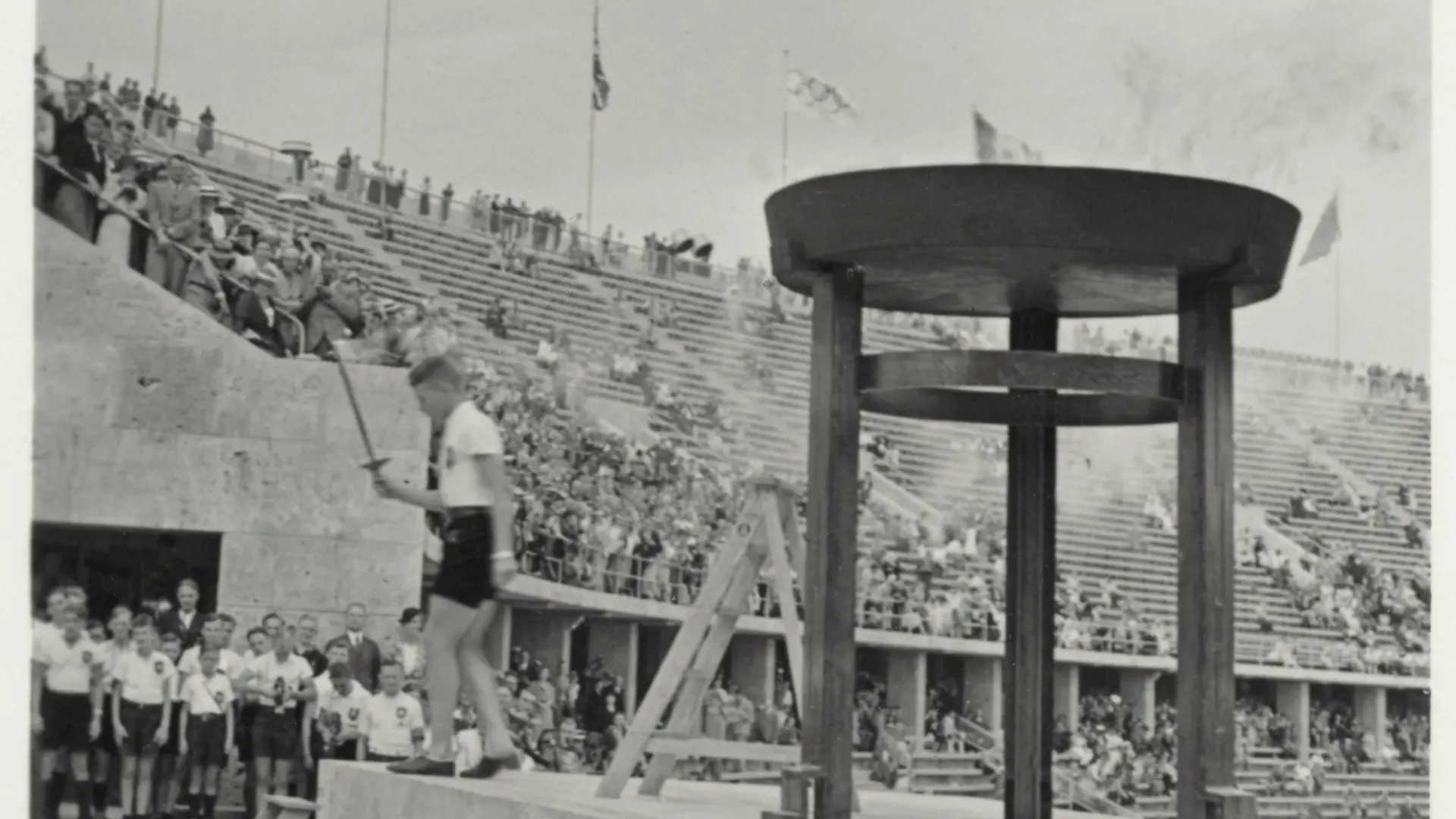 IX. Olympische Spiele / Sommerspiele / Berlin, 1. August bis 16. August 1936 / Staffellauf der Berliner Sportjugend zum Austragungsort der olympischen Ruder- und Kanuten-Wettbewerbe in Grünau, 7. August. - "Berlin: Die Jugend holt das Olympische Feuer zum Staffellauf nach Grünau". - (Entzünden der ersten Fackel an der Olympischen Flamme über dem Marathon-Tor im Berliner Olympiastadion). Foto (Teil einer stereoskopische Aufnahme) von Heinrich Hoffmann (1885-1957). Aus: Die Olympischen Spiele 1936. 100 Raumbild-Aufnahmen von Heinrich Hoffmann. Text von Ludwig Haymann, Diessen am Ammersee (Raumbild-Verlag Otto Schönstein) 1936, Nr. 43. Privatsammlung.
