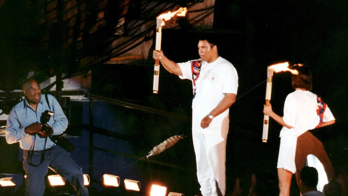 ARCHIV - Der ehemalige Schwergewichts-Boxweltmeister Muhammad Ali (M) hält während der Eröffnungszeremonie der XXVI. Olympischen Sommerspiele in Atlanta eine Fackel in die Höhe und entzündet während der Eröffnungszeremonie der XXVI. Olympischen Sommerspiele in Atlanta das olympische Feuer (Archivfoto vom 20.7.1996). Rechts die Schwimmerin Janet Evans, die als letzte Staffelläuferin das Feuer an Ali übergab. Muhammad Ali, 1942 in Louisville/Kentucky geboren, feiert am 17.01.2007 seinen 65. Geburtstag. Foto: Marttii Kainulainen (zu dpa-KORR.: "Der «Größte» feiert klein: Boxlegende Muhammad Ali wird 65" vom 12.01.2007) +++(c) dpa - Bildfunk+++