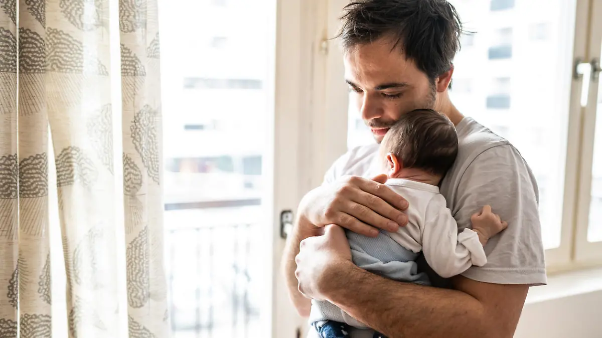 Young modern father embracing newborn baby boy at home on day