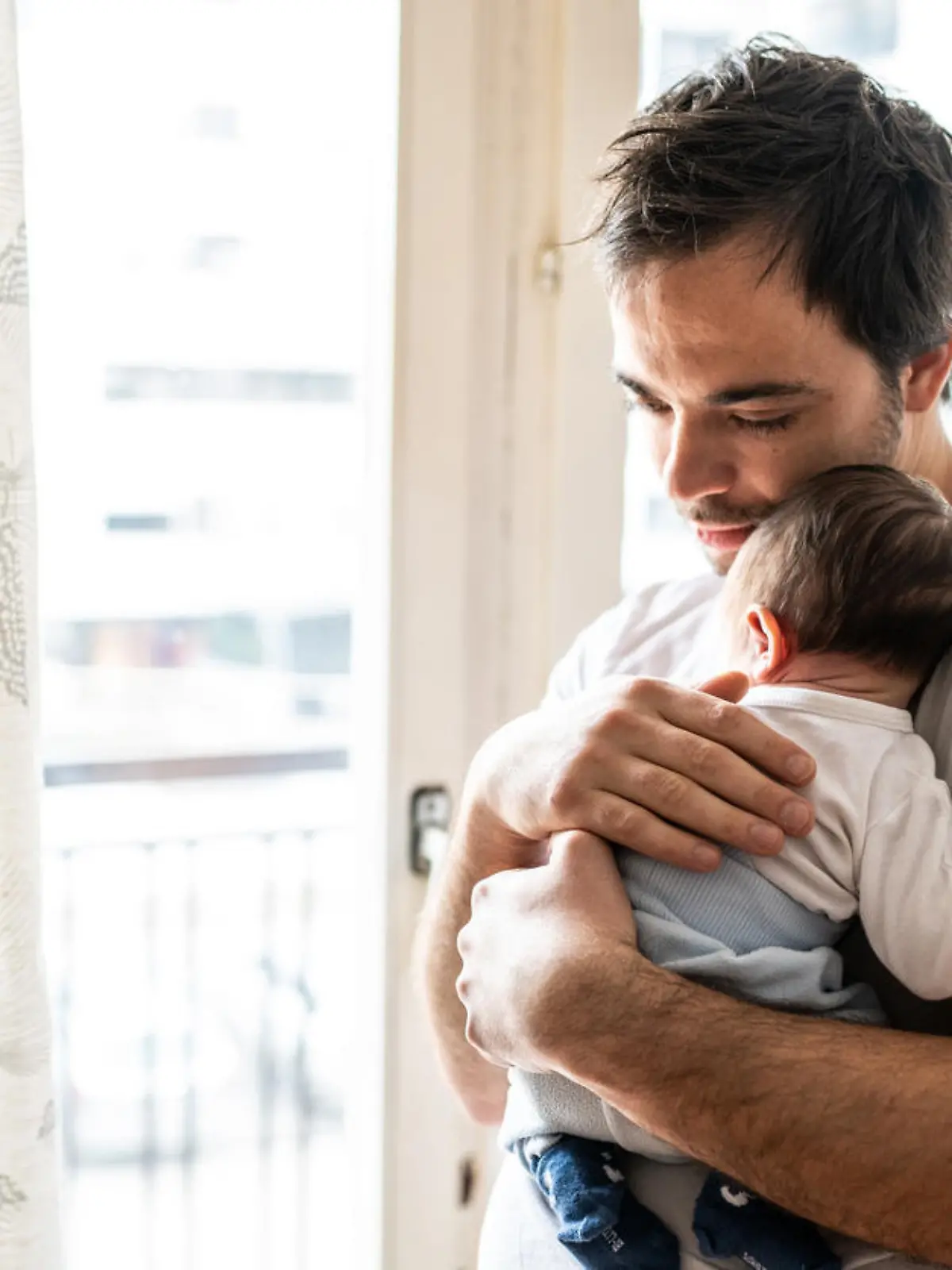 Young modern father embracing newborn baby boy at home on day