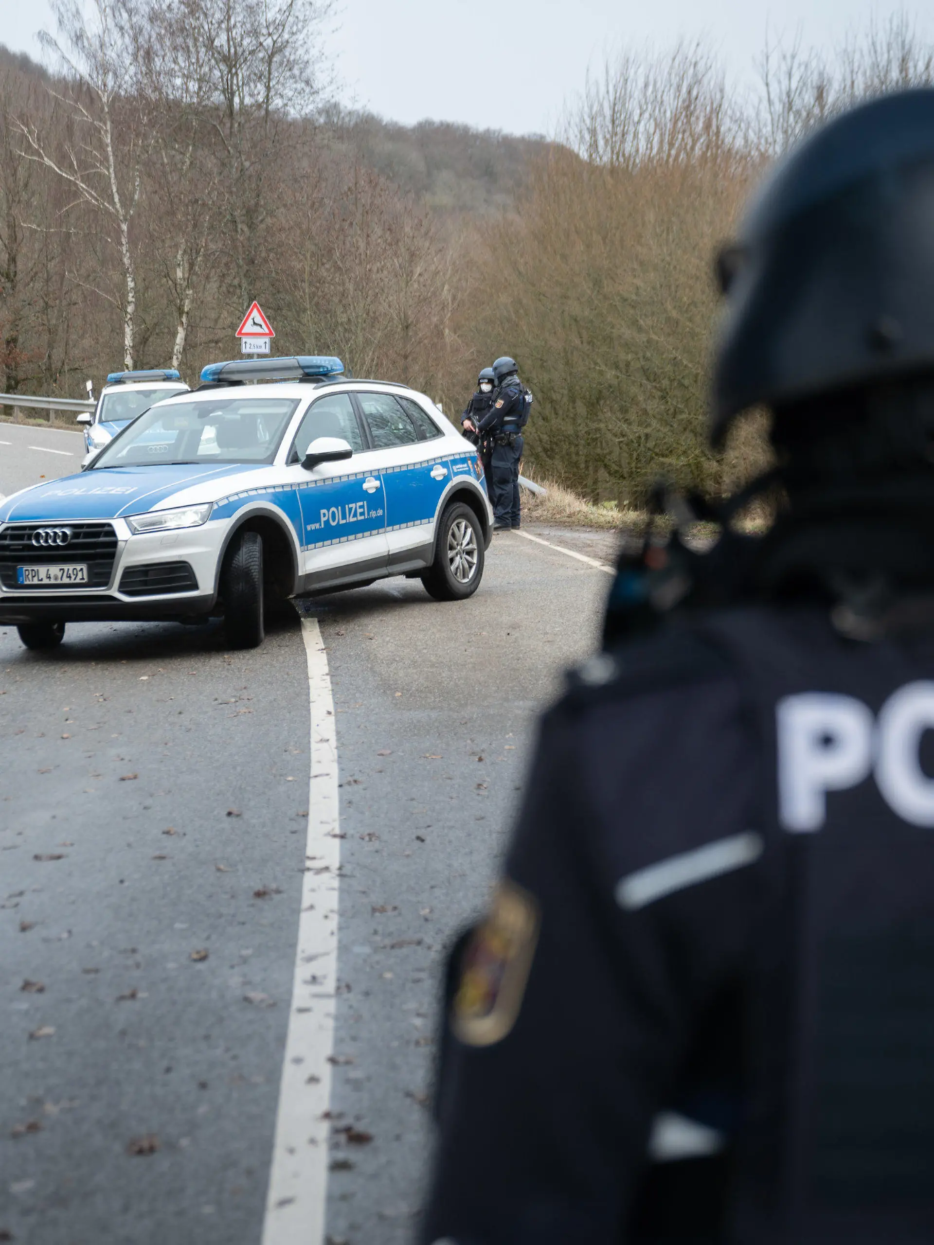 31.01.2022, Rheinland-Pfalz, Mayweilerhof: Polizeibeamte stehen an einer Absperrung an der Kreisstraße 22 rund einen Kilometer von dem Tatort, an dem zwei Polizeibeamte durch Schüsse getötet wurden. Foto: Sebastian Gollnow/dpa +++ dpa-Bildfunk +++