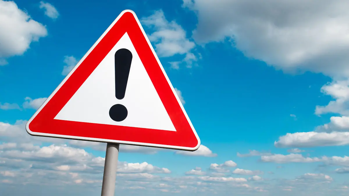 Warning road sign against a cloudy sky.