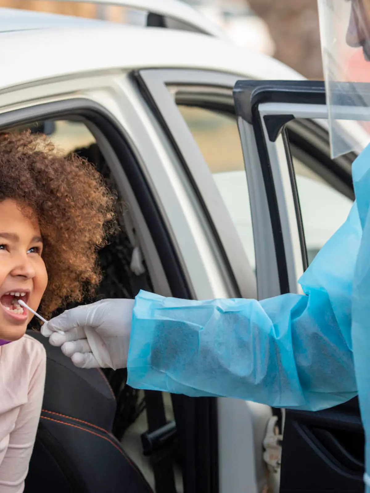 7 years old child getting tested for covid 19. A healthcare worker performing the covid-19 test on a kid patient in a drive-through coronavirus testing station.