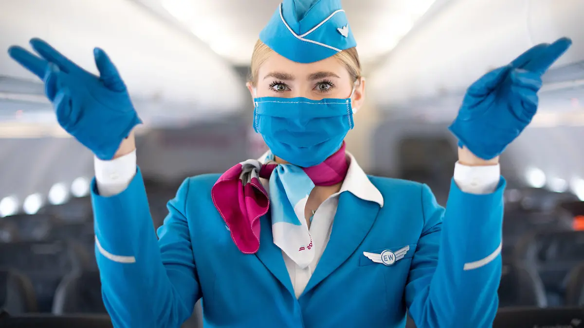 27.05.2020, Nordrhein-Westfalen, Köln: Eine Flugbegleiterin mit Mund-Nasen-Schutz steht während eines Pressetermins in der Kabine eines Flugzeugs von Eurowings und zeigt die Notausgänge. Der Flughafen Köln/Bonn und die Fluggesellschaft Eurowings informierten über erweiterte Gesundheits- und Hygienestandards. Foto: Marius Becker/dpa +++ dpa-Bildfunk +++