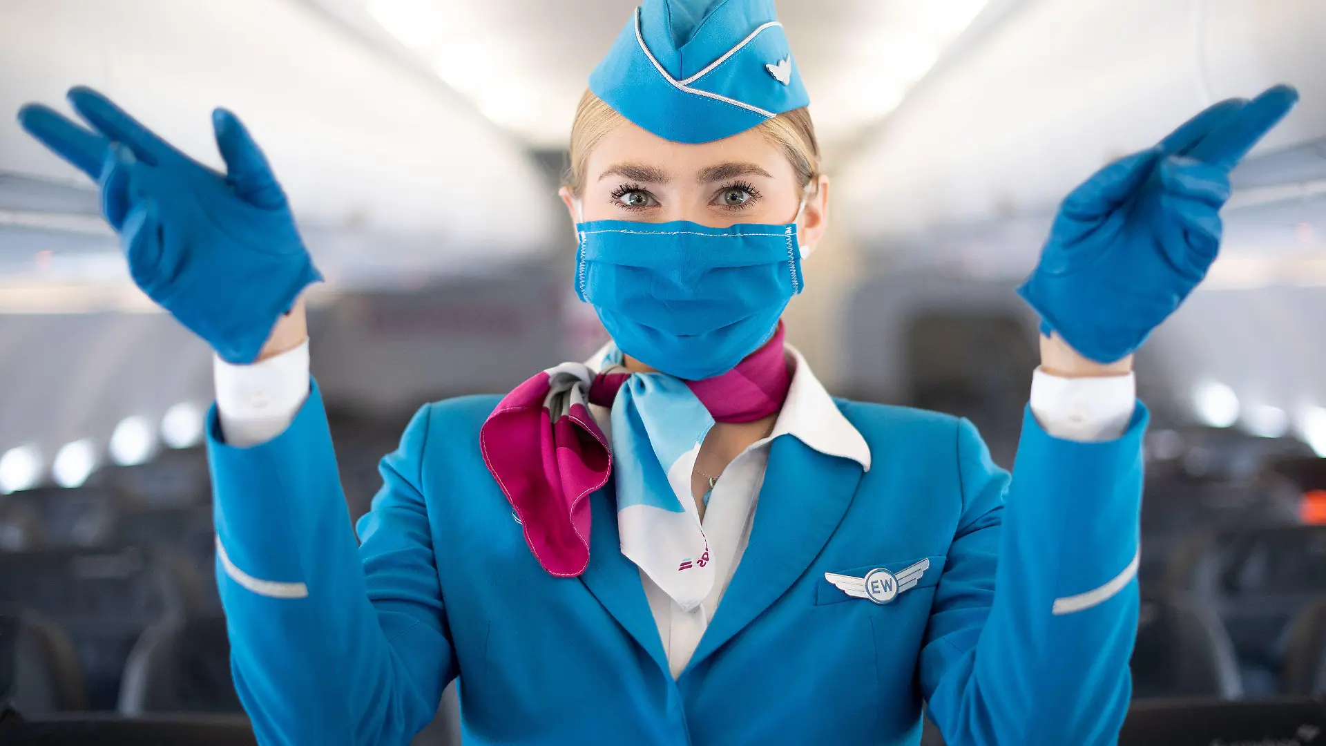 27.05.2020, Nordrhein-Westfalen, Köln: Eine Flugbegleiterin mit Mund-Nasen-Schutz steht während eines Pressetermins in der Kabine eines Flugzeugs von Eurowings und zeigt die Notausgänge. Der Flughafen Köln/Bonn und die Fluggesellschaft Eurowings informierten über erweiterte Gesundheits- und Hygienestandards. Foto: Marius Becker/dpa +++ dpa-Bildfunk +++