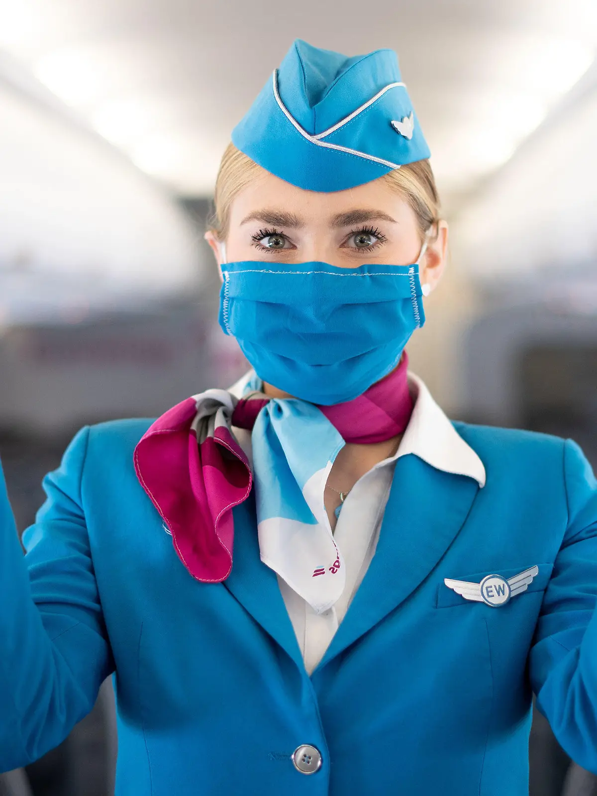 27.05.2020, Nordrhein-Westfalen, Köln: Eine Flugbegleiterin mit Mund-Nasen-Schutz steht während eines Pressetermins in der Kabine eines Flugzeugs von Eurowings und zeigt die Notausgänge. Der Flughafen Köln/Bonn und die Fluggesellschaft Eurowings informierten über erweiterte Gesundheits- und Hygienestandards. Foto: Marius Becker/dpa +++ dpa-Bildfunk +++