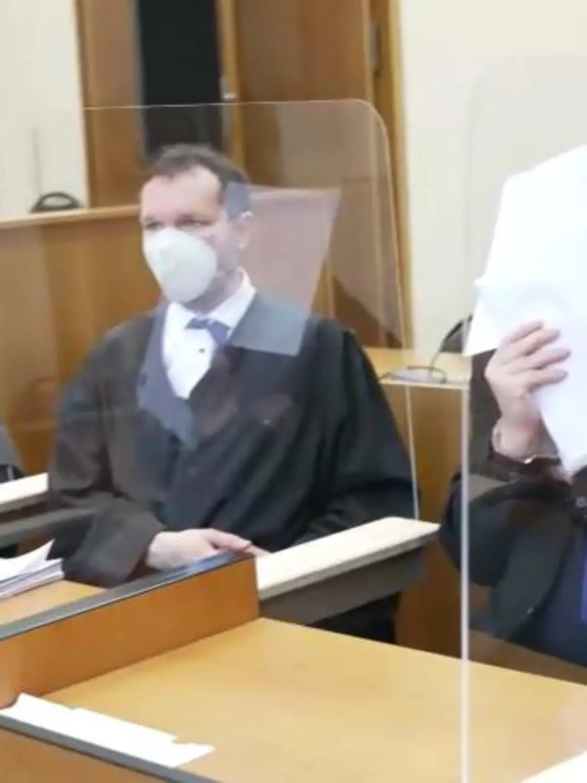 Zwei Männer im Gerichtssaal, einer hält sich Papier vor das Gesicht.