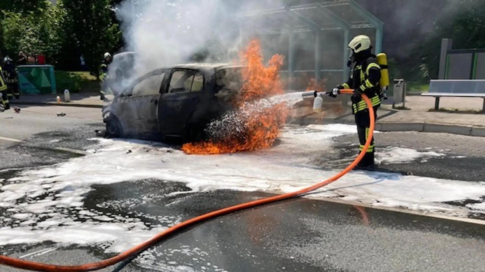Die Feuerwehr löscht einen brennenden Kleinwagen auf einer Straße.
