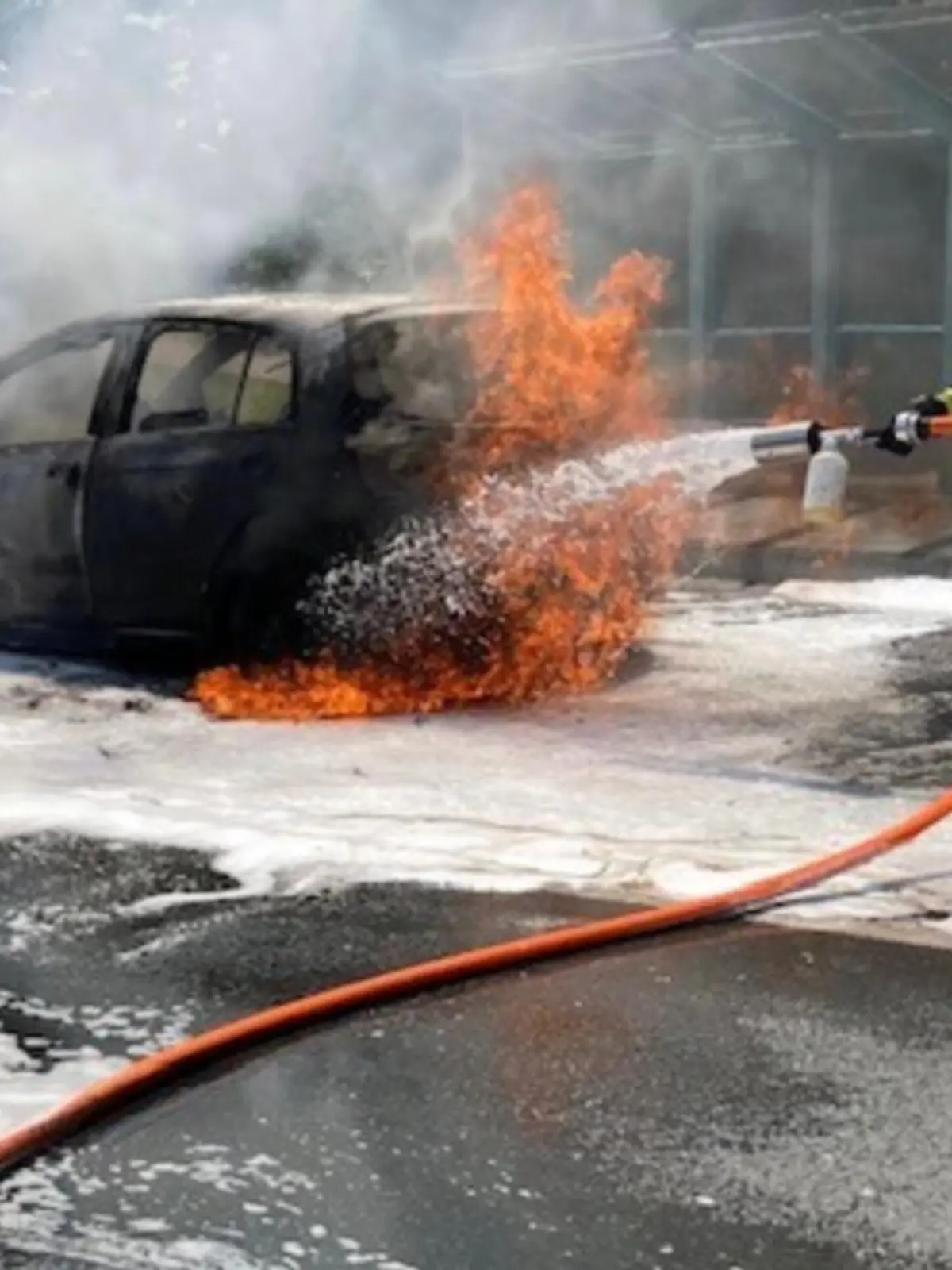 Die Feuerwehr löscht einen brennenden Kleinwagen auf einer Straße.
