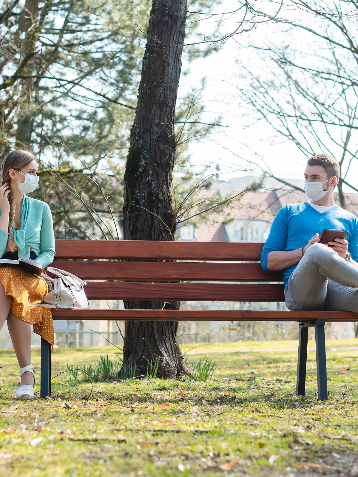 Woman and man with face mask in social distancing flirting sitting on a park bench