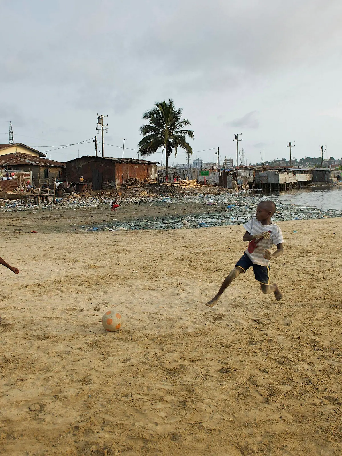 Children play soccer (football) on sandy beach behind the West Point slum in Monrovia, the capital of Liberia. The West Point Township or slum in Monrovia houses over 70,000 people. It is known to be one of the most dangerous slums in Monrovia. Water and sanitation condition in the slum is certainly less that adequate. Due to the lack of sanitary latrines, it is common for many residents of the West Point to defecate in open near the beach. It is also common for people to dispose of garbage on the beach that continues to create health hazards for its residents. In recent times, Liberia continues to recover from a ruinous 14-year civil war that ended in 2003. Although the Government is working to rebuild the countryÄôs destroyed infrastructure, many Liberians still live without access to basic services. The influx of approximately 178,000 refugees from Cv¥te d'Ivoire, who fled their own country after controversy surrounding the 28 November 2010 presidential election turned violent, has only exacerbated the situation. Waning supplies of safe drinking water and food, inadequate sanitation facilities, constricted access to medical care and overcrowding all threaten the health of Liberian and Ivorian children alike. The education of many children has also been disrupted because refugees stay in schools when there are not enough families to host them. The poor condition of roads makes it difficult for aid to reach remote areas, where many of the most vulnerable families live. Many of the refugees have returned home, but thousands have stayed back, often hosted by Liberian communities and families, both in rural and urban areas of the country. NGOs and the Liberian Government continue to work hard to provide life-saving services for both Liberian citizens and Ivorian refugees.