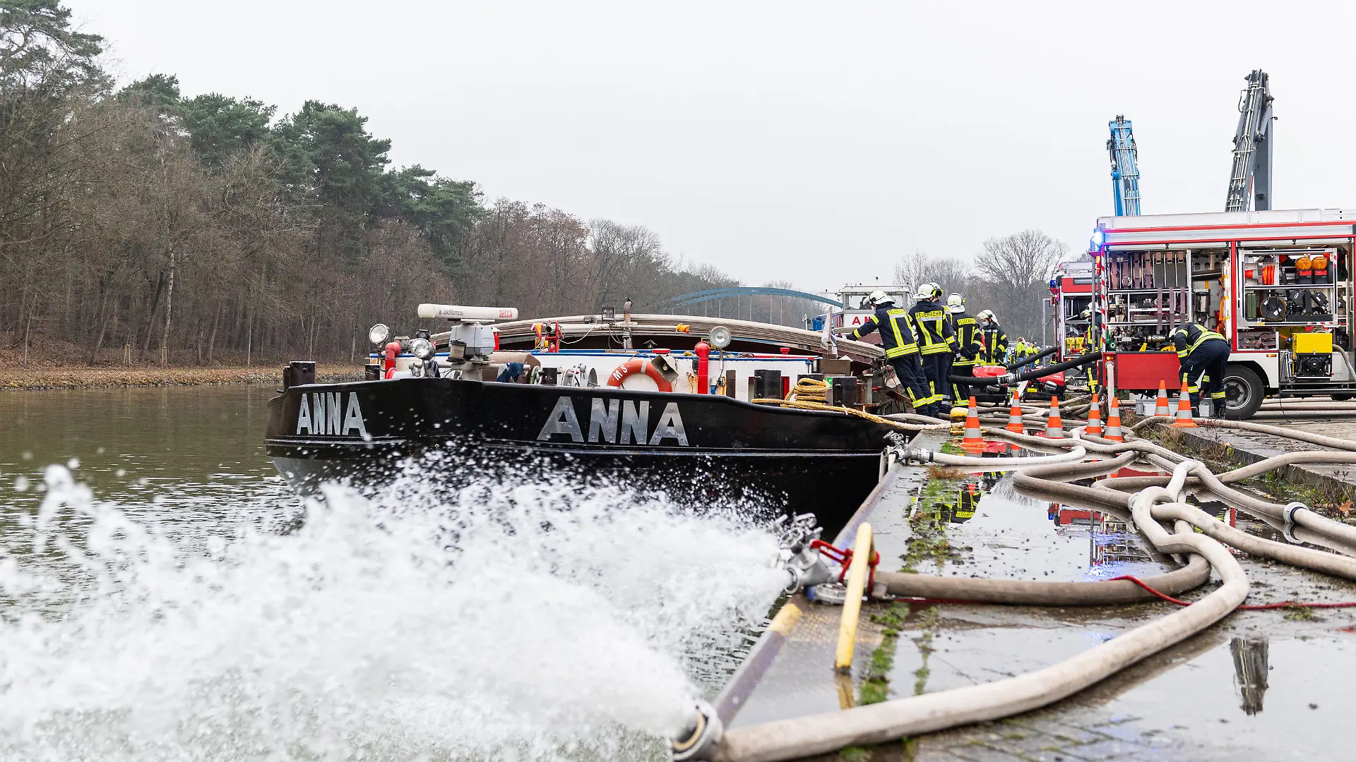 25.01.2022, Niedersachsen, Spelle: Die Feuerwehr pumpt ein mit Wasser vollgelaufenes Binnenschiff, dass an einer Keilmauer auf dem Dortmund-Ems Kanal liegt mit insgesamt vier Pumpen leer. Treibstoff ist aus dem Dieseltank des 80m langen Schiffs ausgelaufen und Wasser ist in den Laderaum eingedrungen, wobei das Schiff mit dem kompletten Bug unter Wasser stand. Foto: Guido Kirchner/dpa +++ dpa-Bildfunk +++