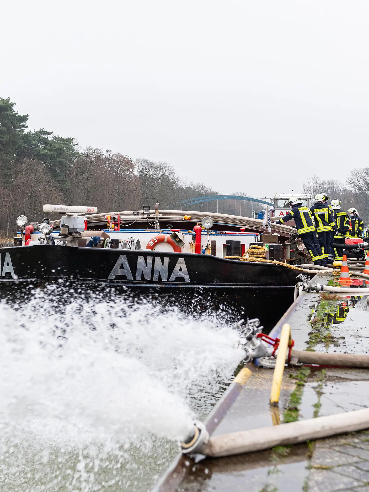25.01.2022, Niedersachsen, Spelle: Die Feuerwehr pumpt ein mit Wasser vollgelaufenes Binnenschiff, dass an einer Keilmauer auf dem Dortmund-Ems Kanal liegt mit insgesamt vier Pumpen leer. Treibstoff ist aus dem Dieseltank des 80m langen Schiffs ausgelaufen und Wasser ist in den Laderaum eingedrungen, wobei das Schiff mit dem kompletten Bug unter Wasser stand. Foto: Guido Kirchner/dpa +++ dpa-Bildfunk +++