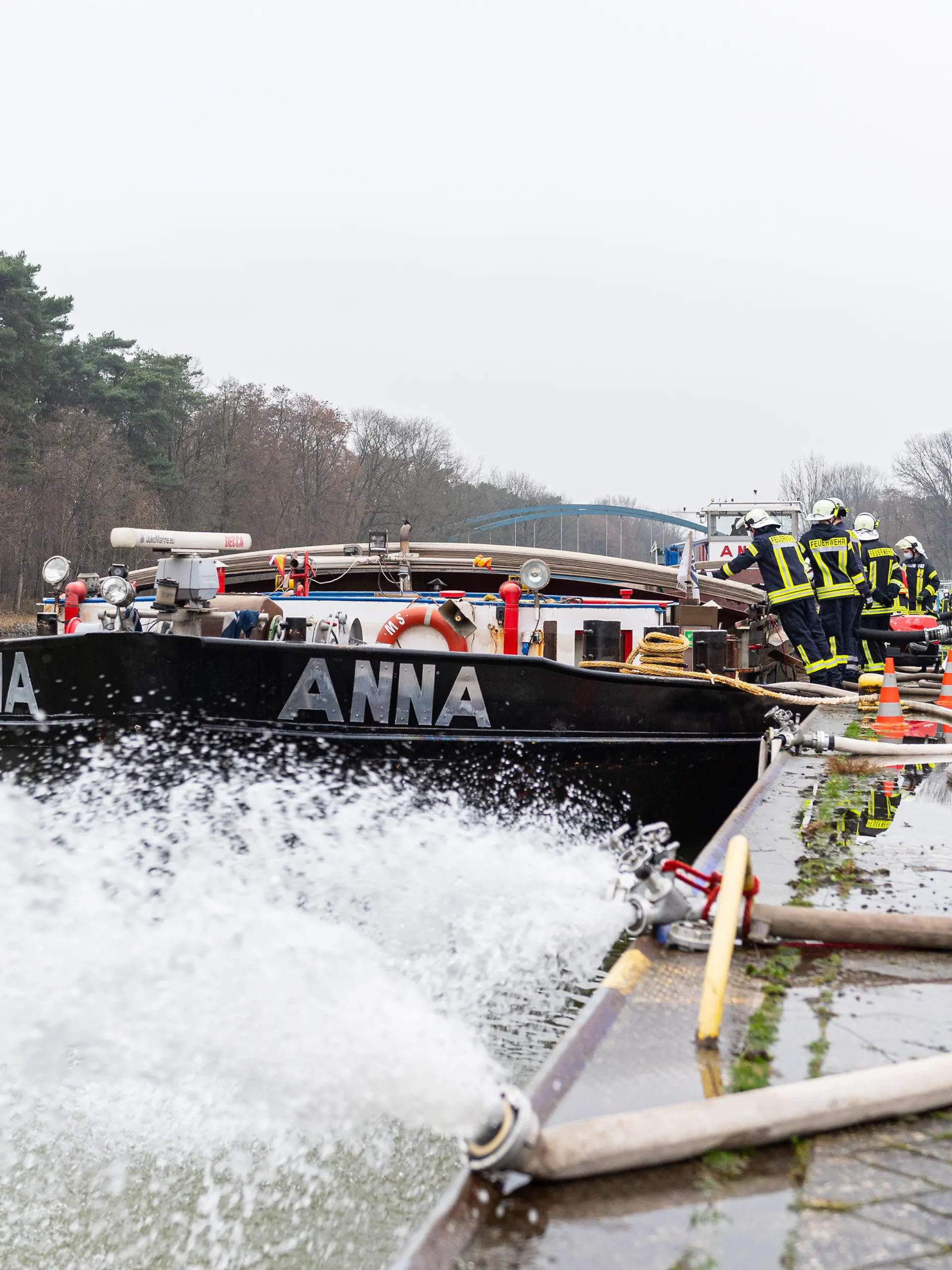 25.01.2022, Niedersachsen, Spelle: Die Feuerwehr pumpt ein mit Wasser vollgelaufenes Binnenschiff, dass an einer Keilmauer auf dem Dortmund-Ems Kanal liegt mit insgesamt vier Pumpen leer. Treibstoff ist aus dem Dieseltank des 80m langen Schiffs ausgelaufen und Wasser ist in den Laderaum eingedrungen, wobei das Schiff mit dem kompletten Bug unter Wasser stand. Foto: Guido Kirchner/dpa +++ dpa-Bildfunk +++