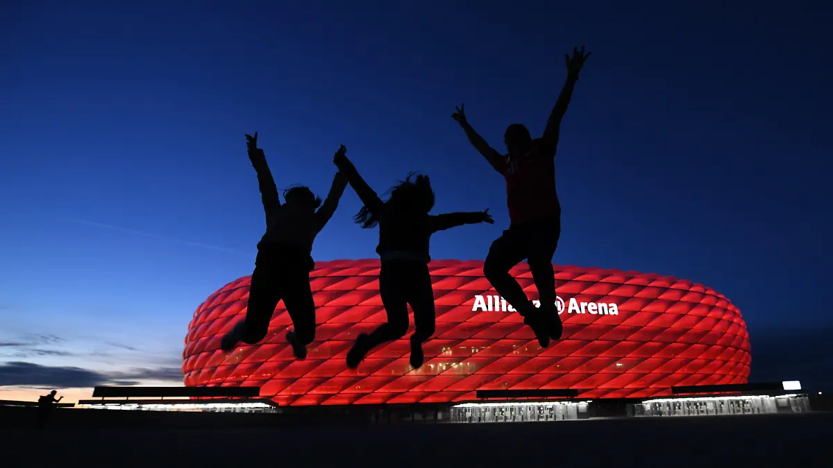 08.05.2021, Bayern, München: Drei Fans springen nach der Partie in der Fußball Bundesliga FC Bayern München - Borussia Mönchengladbach vor der Allianz Arena in die Höhe. Einige Fans haben sich vor dem Stadion versammelt. Die neuen Corona-Bestimmungen für Einreisen aus Großbritannien könnten auch dem EM-Spielort München Sorgen bringen. Sollten die verschärften Maßnahmen bis Anfang Juli gültig bleiben und die UEFA als Turnier-Ausrichter keine Ausnahme erwirken, wäre das Viertelfinale in der Allianz Arena am 2. Juli in Gefahr. Einer der Teilnehmer des K.o.-Spiels hätte zuvor sein Achtelfinale in London ausgetragen und dürfte dann womöglich nicht einreisen. Die Europäische Fußball-Union teilte am Mittwoch mit, sie prüfe die Lage. (zu dpa «Verschärfte Einreise-Regeln: EM-Viertelfinale in München in Gefahr?») Foto: Tobias Hase/dpa +++ dpa-Bildfunk +++