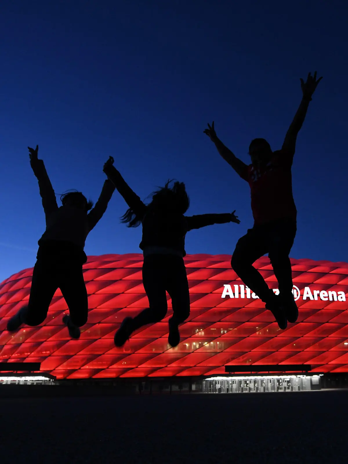 08.05.2021, Bayern, München: Drei Fans springen nach der Partie in der Fußball Bundesliga FC Bayern München - Borussia Mönchengladbach vor der Allianz Arena in die Höhe. Einige Fans haben sich vor dem Stadion versammelt. Die neuen Corona-Bestimmungen für Einreisen aus Großbritannien könnten auch dem EM-Spielort München Sorgen bringen. Sollten die verschärften Maßnahmen bis Anfang Juli gültig bleiben und die UEFA als Turnier-Ausrichter keine Ausnahme erwirken, wäre das Viertelfinale in der Allianz Arena am 2. Juli in Gefahr. Einer der Teilnehmer des K.o.-Spiels hätte zuvor sein Achtelfinale in London ausgetragen und dürfte dann womöglich nicht einreisen. Die Europäische Fußball-Union teilte am Mittwoch mit, sie prüfe die Lage. (zu dpa «Verschärfte Einreise-Regeln: EM-Viertelfinale in München in Gefahr?») Foto: Tobias Hase/dpa +++ dpa-Bildfunk +++