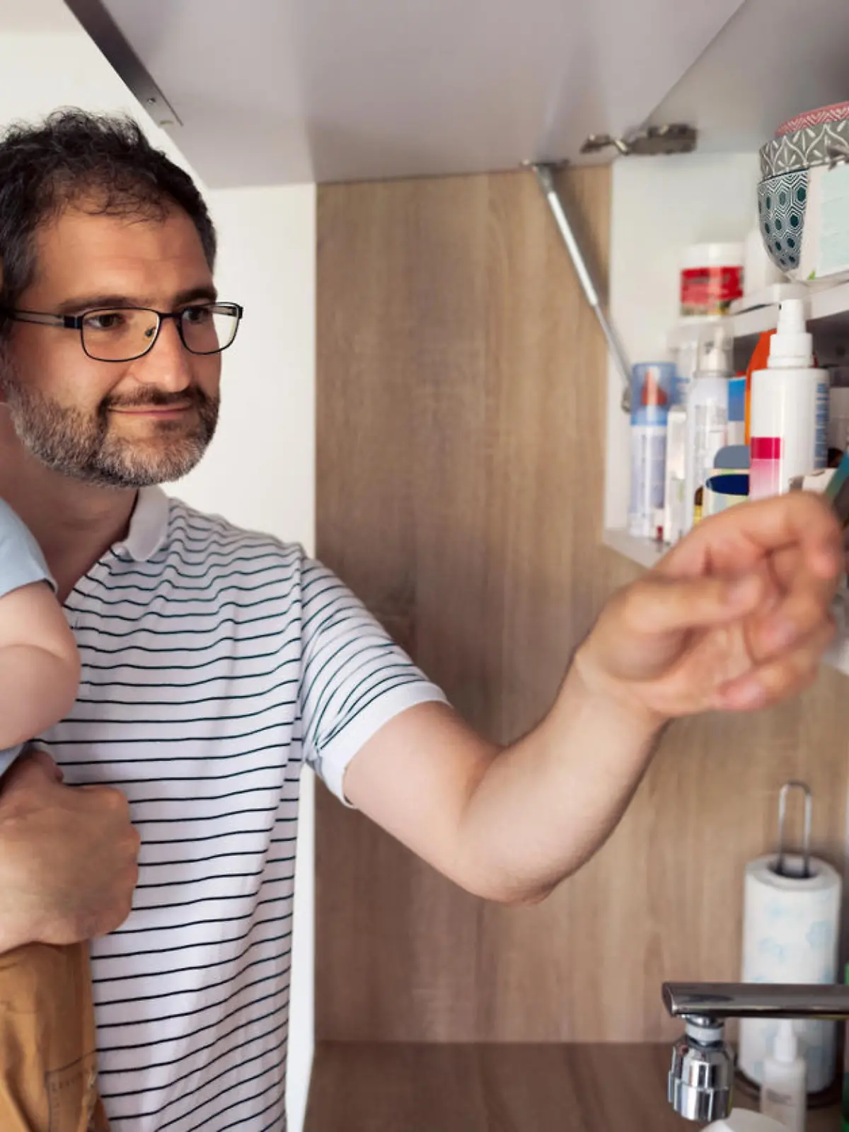 Caucasian mature adult father and his baby son taking medicines out of medicine cabinet at home.