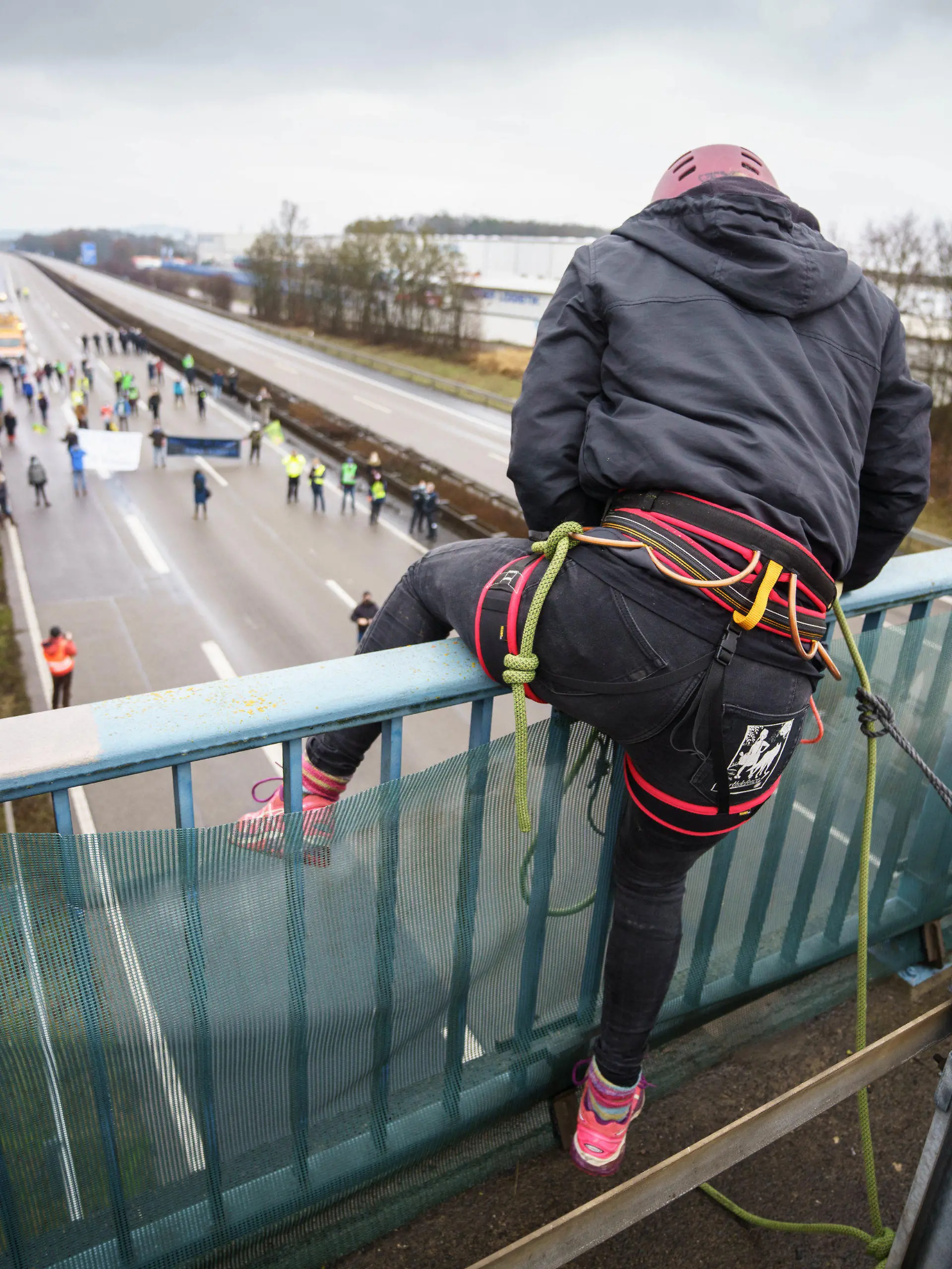 23.01.2022, Hessen, Künzell: Ein Aktivistin klettert über das Geländer einer Brücke über die gesperrte Fahrbahn der Autobahn A7 am Rande von Künzell bei Fulda. Mit der genehmigten Abseilaktionktion soll für eine echte Verkehrswende, den sofortigen Stopp des Straßenbaus, einen konsequenten Klimaschutz und gegen Strafen für Autobahnaktionen geworben werden. Foto: Frank Rumpenhorst/dpa/Frank Rumpenhorst/dpa +++ dpa-Bildfunk +++