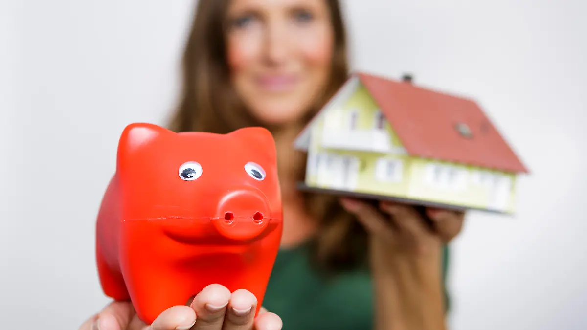ILLUSTRATION - Eine Frau hält am 18.06.2014 in einem Studio in Berlin ein Sparschwein und ein Haus in den Händen.