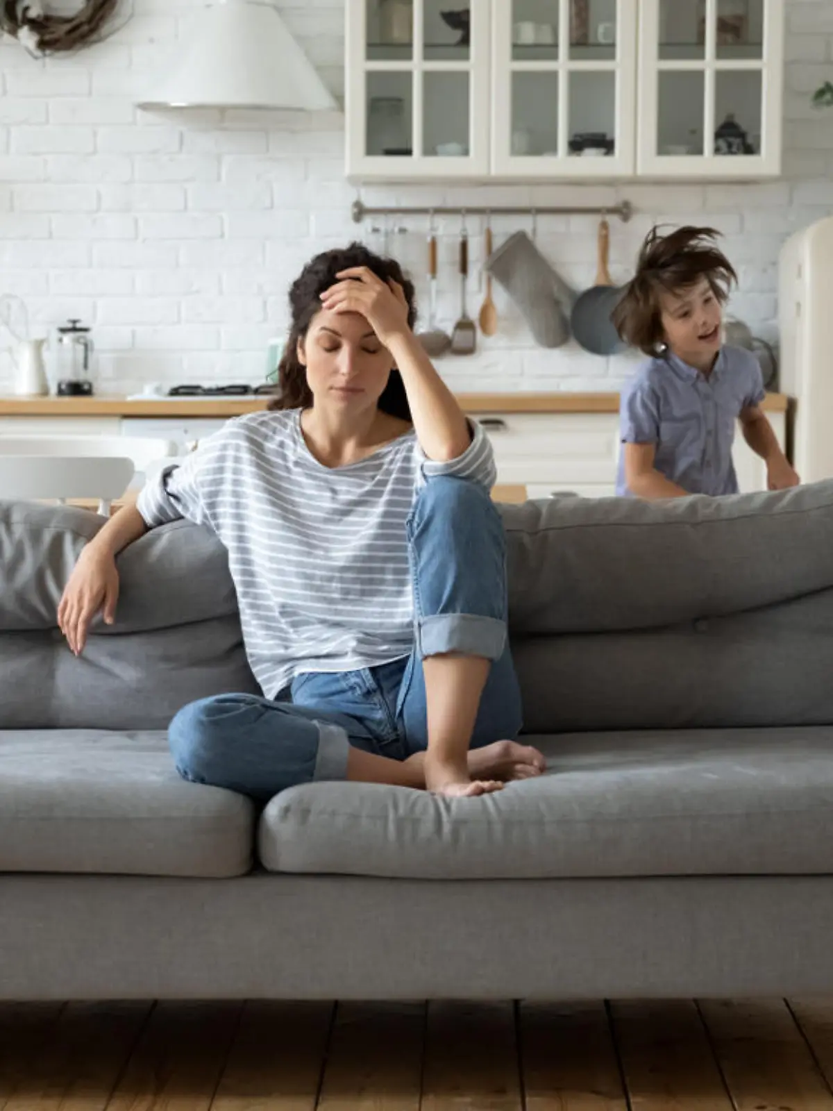 Eine Mutter sitzt gestresst auf einem Sofa.