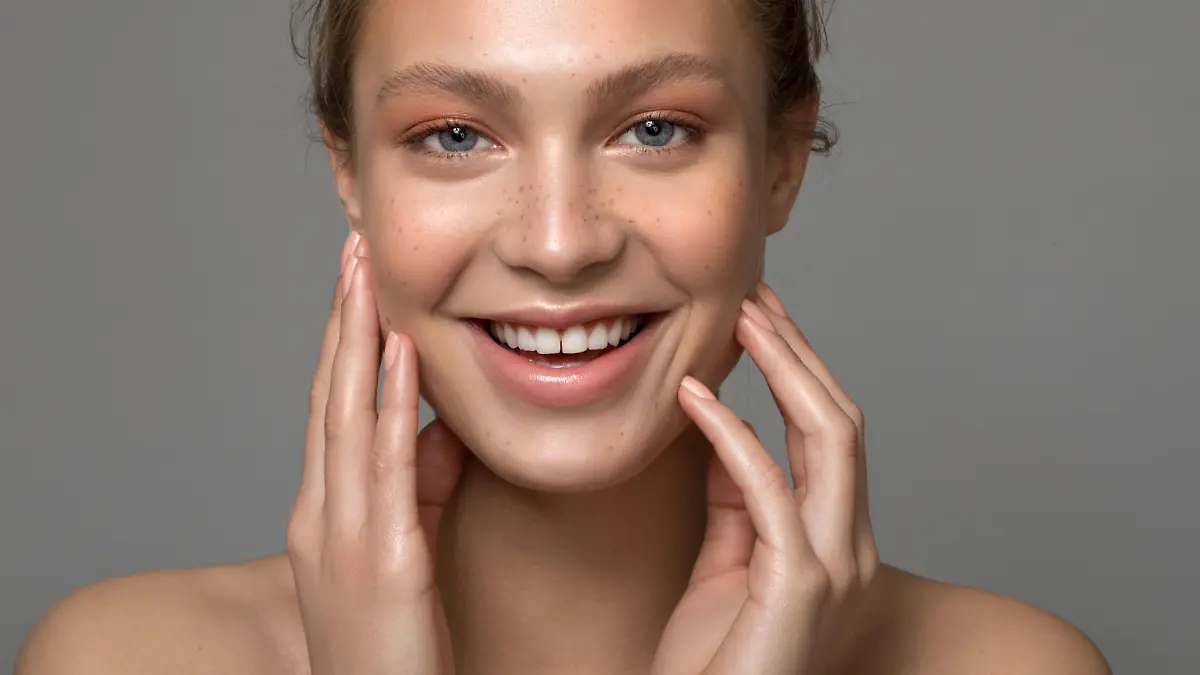 Closeup studio shot of a beautiful young woman with freckles skin posing against a grey background
