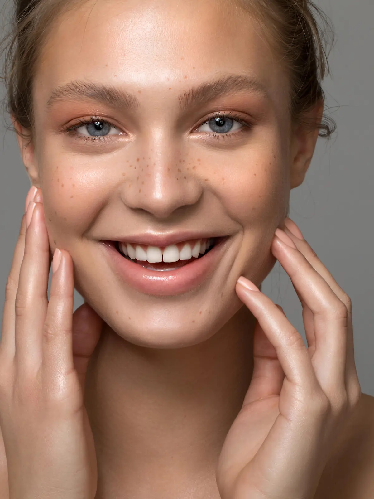 Closeup studio shot of a beautiful young woman with freckles skin posing against a grey background