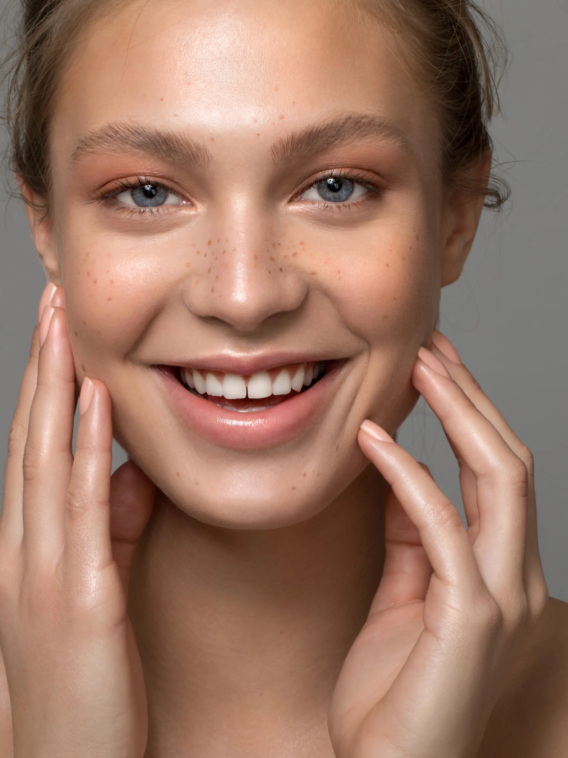 Closeup studio shot of a beautiful young woman with freckles skin posing against a grey background