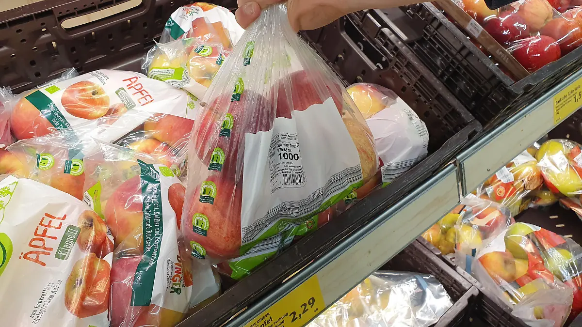 Themenbild - ab 2022 keine Plastiktüte, Plastiktuete, Knotenbeutel, Plastikbeutel im Supermarkt, Discounter mehr erlaubt Bild: Ein Kunde hat einen mit Obst, Gemuese befuellten Plastikbeutel, Beutel, Knotenbeutel, Faltenbeutel an der Obst- und Gemuesetheke iim Supermarkt Edeka in seiner Hand, Finger.