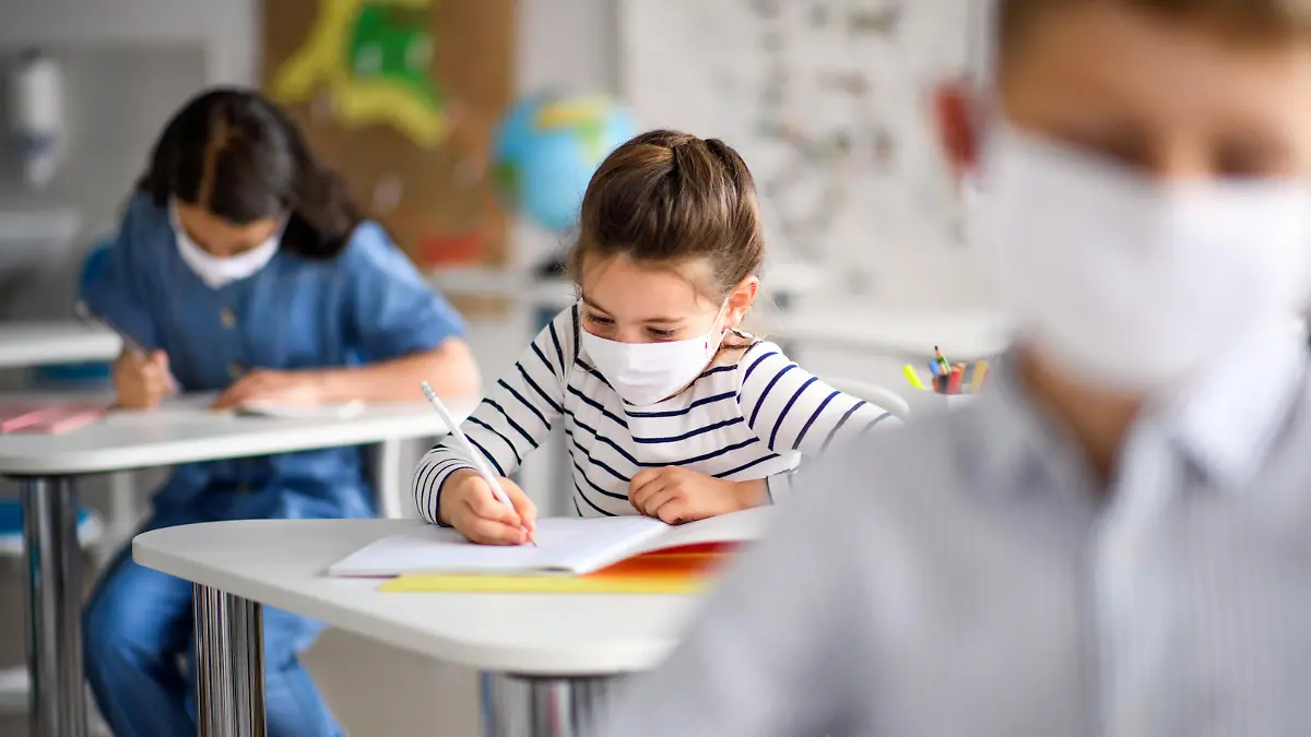 Small children with face mask back at school after covid-19 quarantine and lockdown, writing.