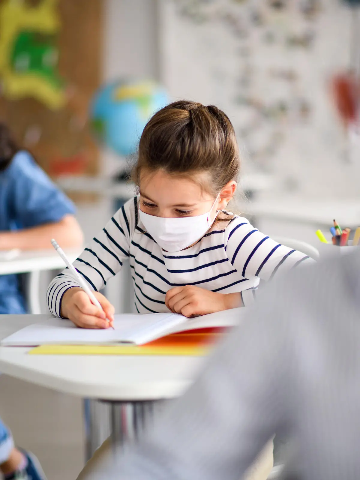 Small children with face mask back at school after covid-19 quarantine and lockdown, writing.