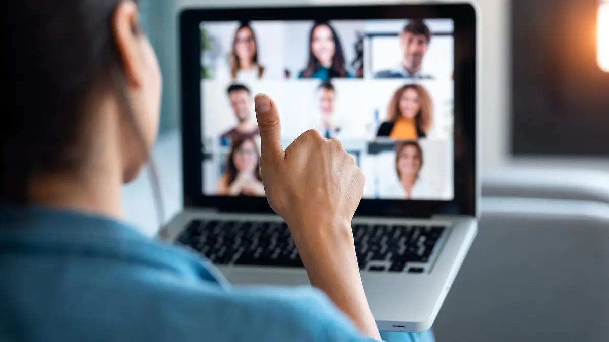 Back view of business woman making video call and showing thumb up to laptop on the online briefing while sit on sofa at home.