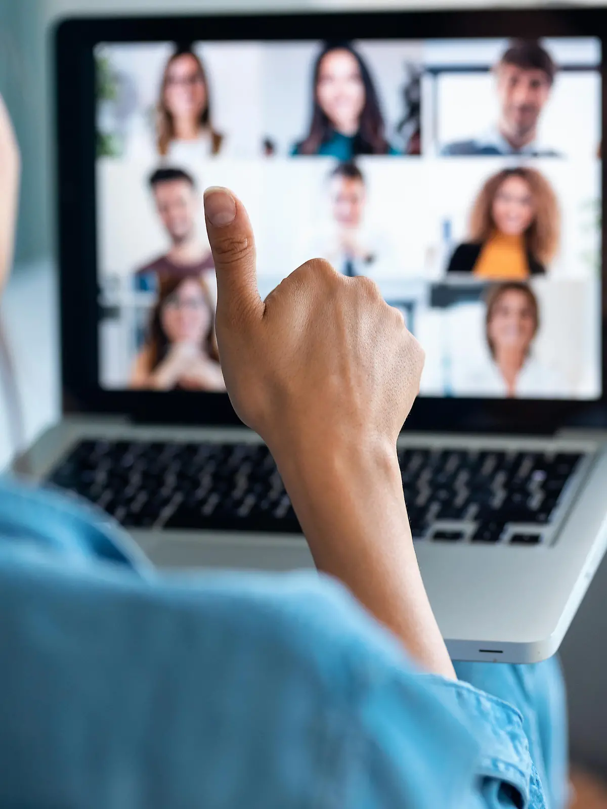 Back view of business woman making video call and showing thumb up to laptop on the online briefing while sit on sofa at home.