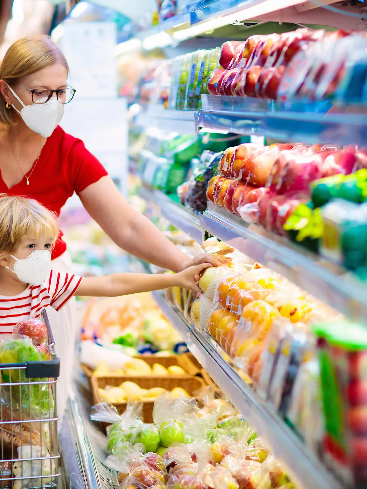 Shopping with kids during virus outbreak. Mother and child wearing surgical face mask buying fruit in supermarket. Mom and little boy buy fresh vegetable in grocery store. Family in shop.