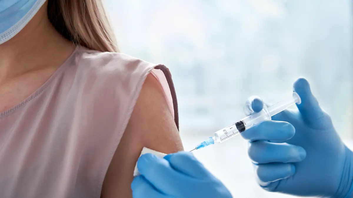 Male doctor holding syringe making covid 19 vaccination injection dose in shoulder of female patient wearing mask. Flu influenza vaccine clinical trials concept, corona virus treatment, close up view.