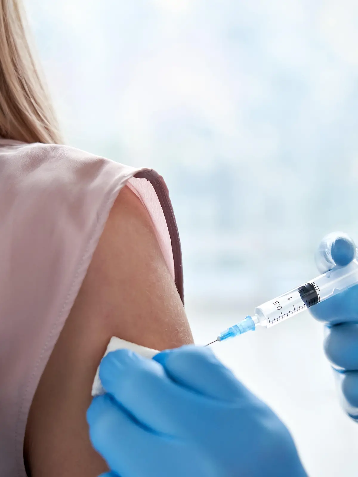 Male doctor holding syringe making covid 19 vaccination injection dose in shoulder of female patient wearing mask. Flu influenza vaccine clinical trials concept, corona virus treatment, close up view.