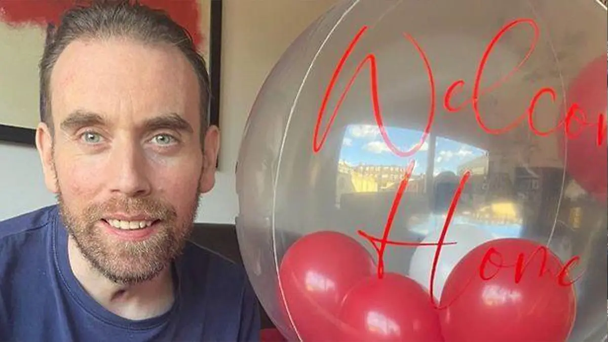 Ein Mann lacht in die Kamera, neben ihm ist ein Luftballon, auf dem "Welcome Home" steht.